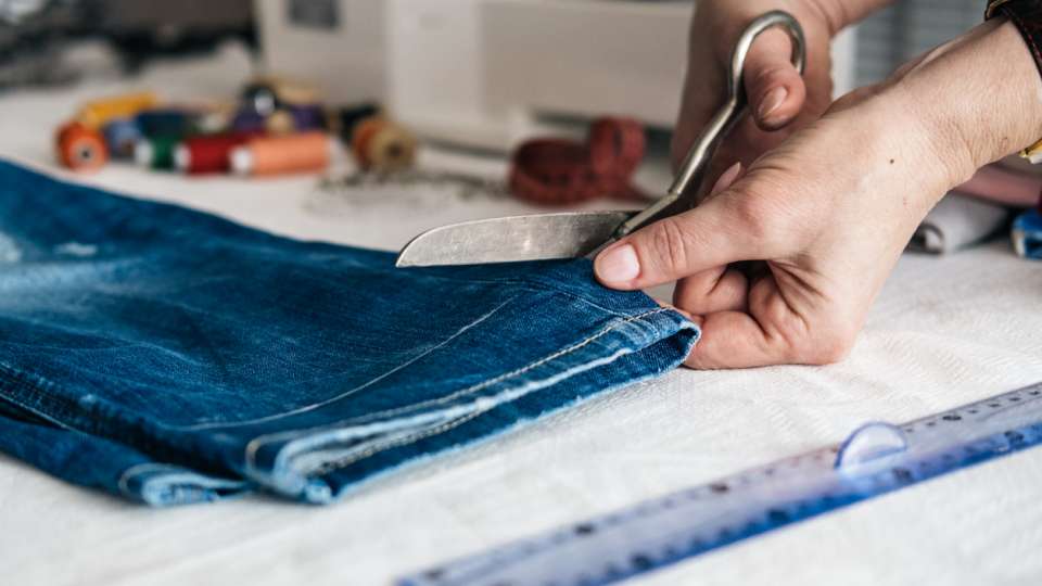 Tailor cutting jeans with scissors at workshop