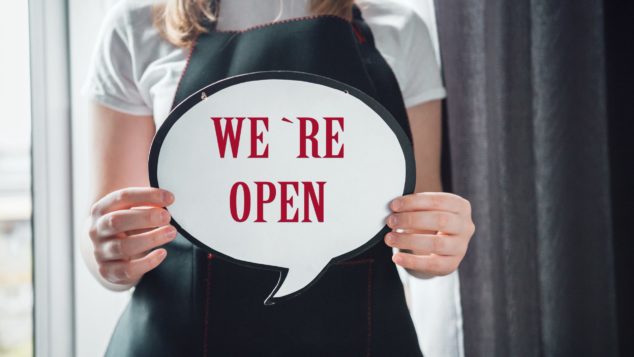 Woman holding 'We're Open' sign, small shops coronavirus concept